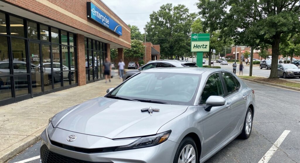 Silver rental car parked outside a Charlotte car rental office with keys on hood, representing temporary transportation after an accident